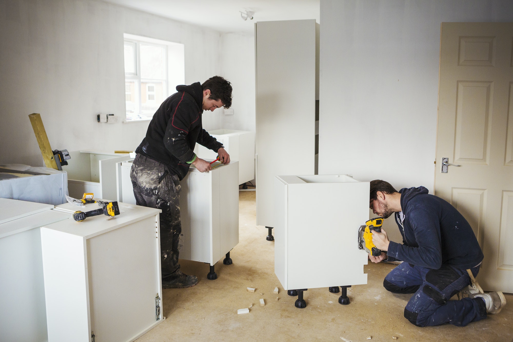 Two builders, building white kitchen units.